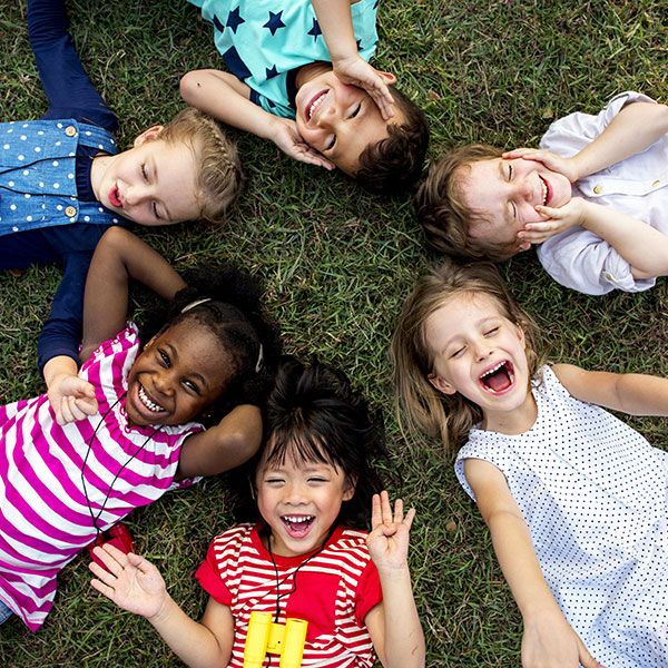 Six children laying in the grass smiling.